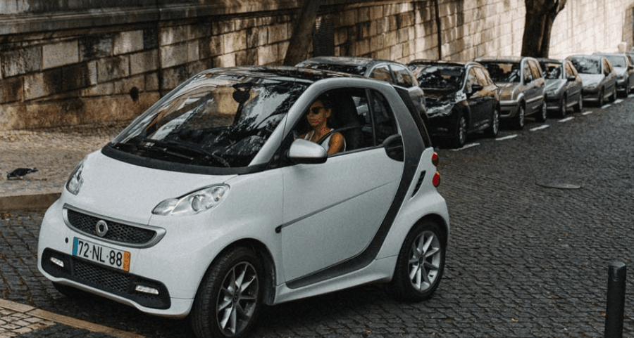 A compact white car driving on a cobblestone street, representing urban mobility and Belgian vehicle taxation.