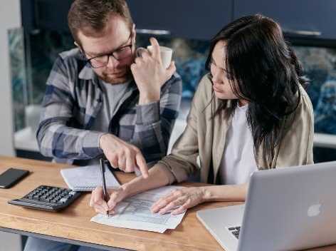 Two business professionals in glasses analyzing technical data on a laptop and paperwork together.